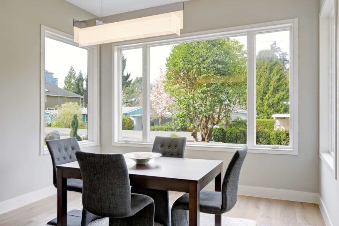 Image depicts a dining room, with a dining table and dining chairs and newly installed vinyl windows.